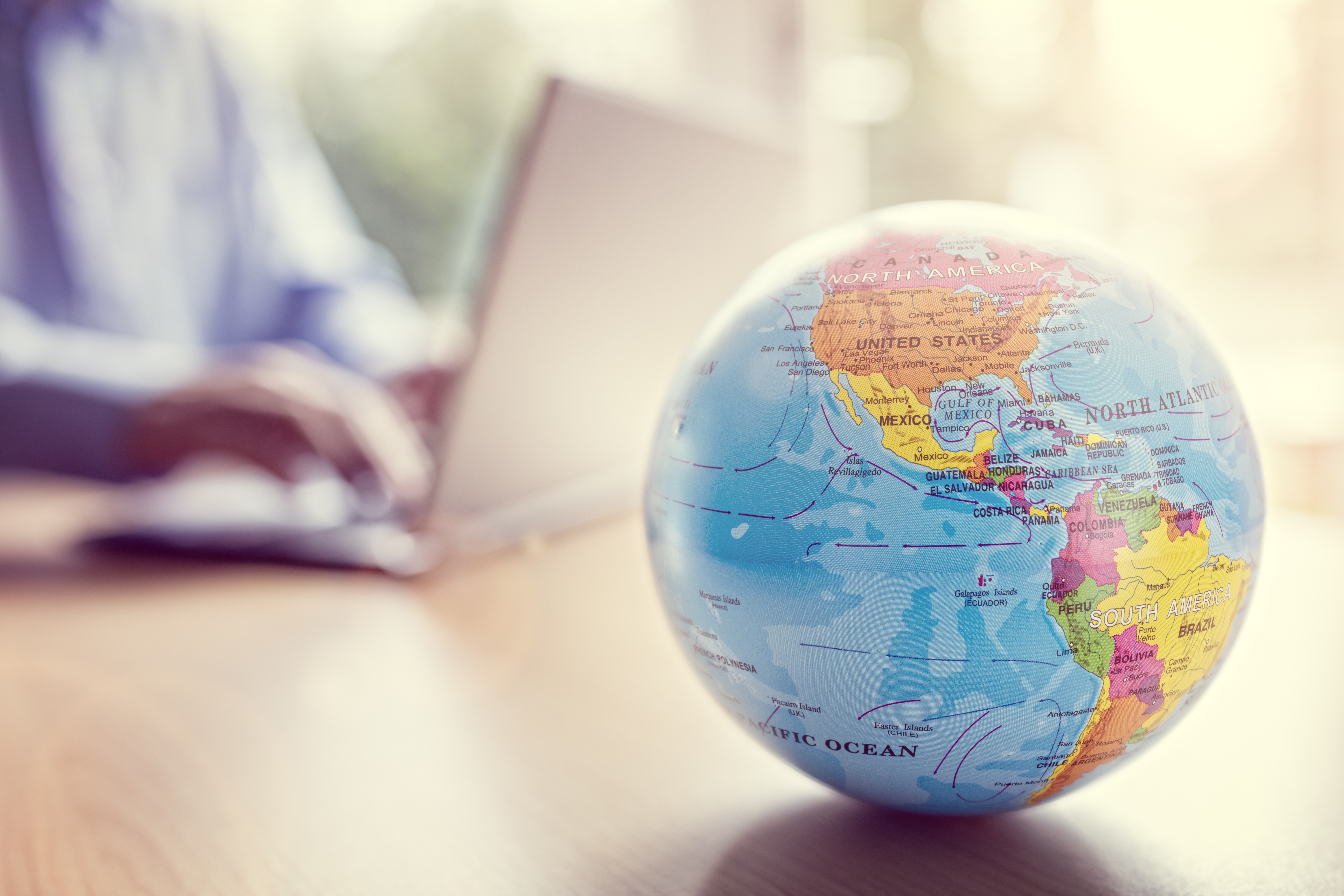 Globe of the Earth in the foreground of the image, with a man on a laptop behind the globe.